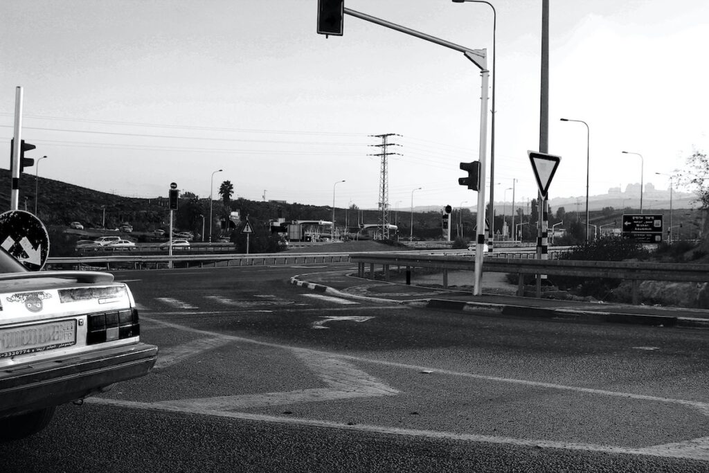 Black and white photo of a road in Israel with the back of a car and Tel Aviv skyline in view