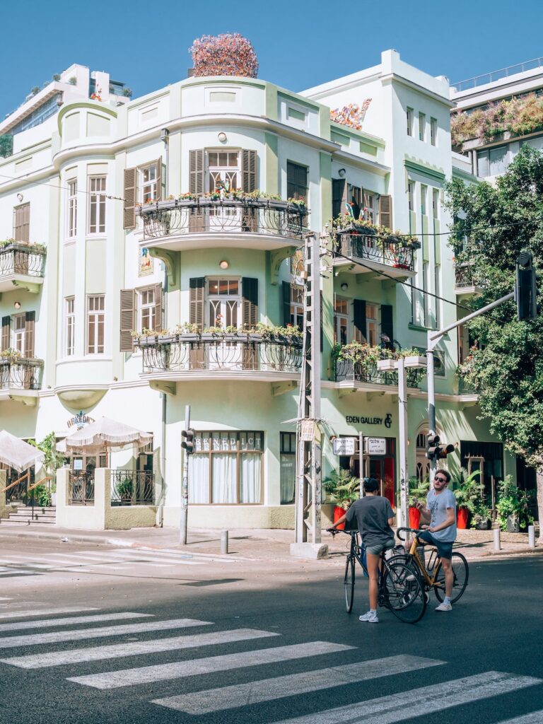 Bikes on a road in Tel Aviv, Israel with a green building that has balconies and plants.