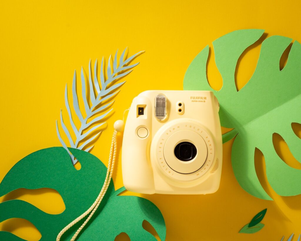 Fujifilm INSTAX Mini 12 in yellow with a flat lay background with yellow and green leaves