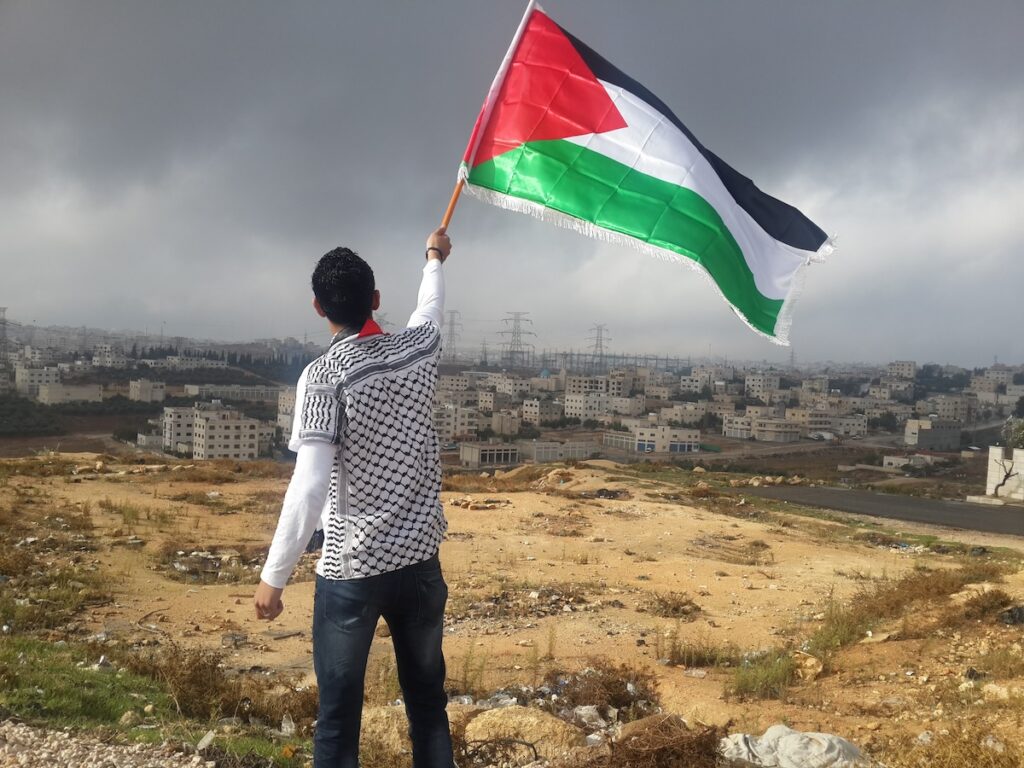 Man holding a Palestinian flag with Palestine in the background